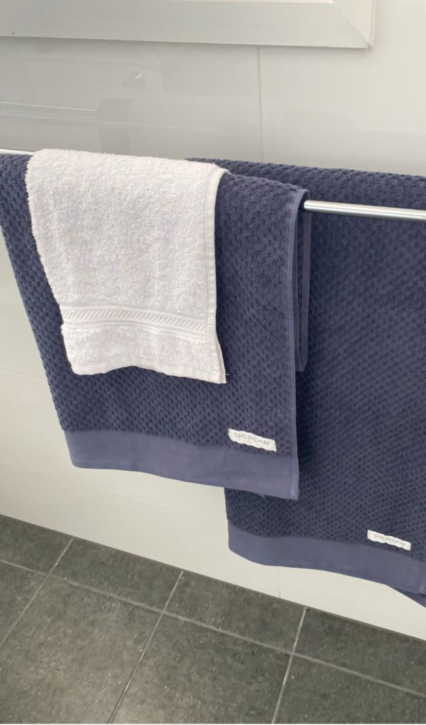 two dark blue bath towels layered with a white facewasher on top