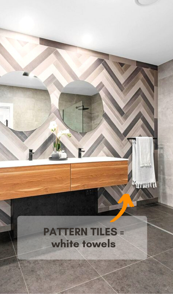 patterned tiles across the entire bathroom wall in a zig-zag pattern with white bath towels hanging near