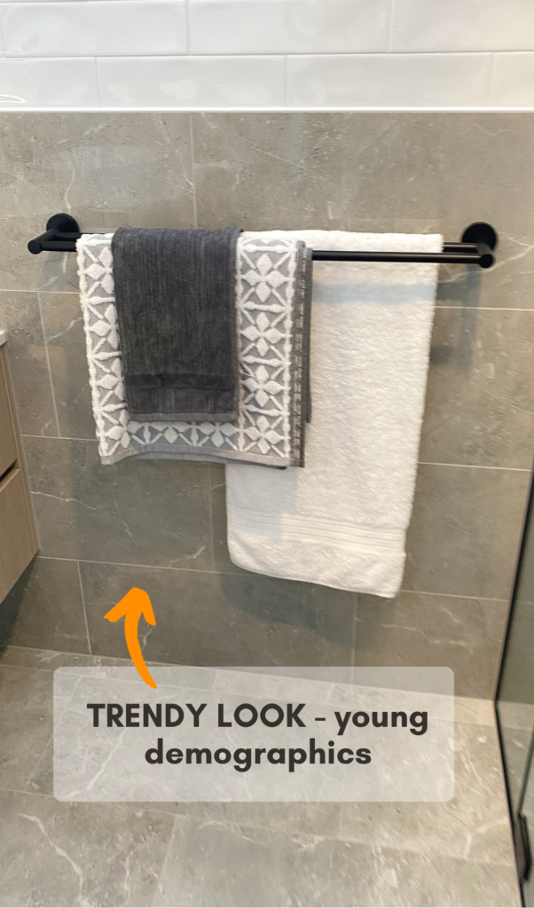 three towels in total, one large white bath towel ona rack, above it is a patterned grey hand towel with a dark blue facewasher