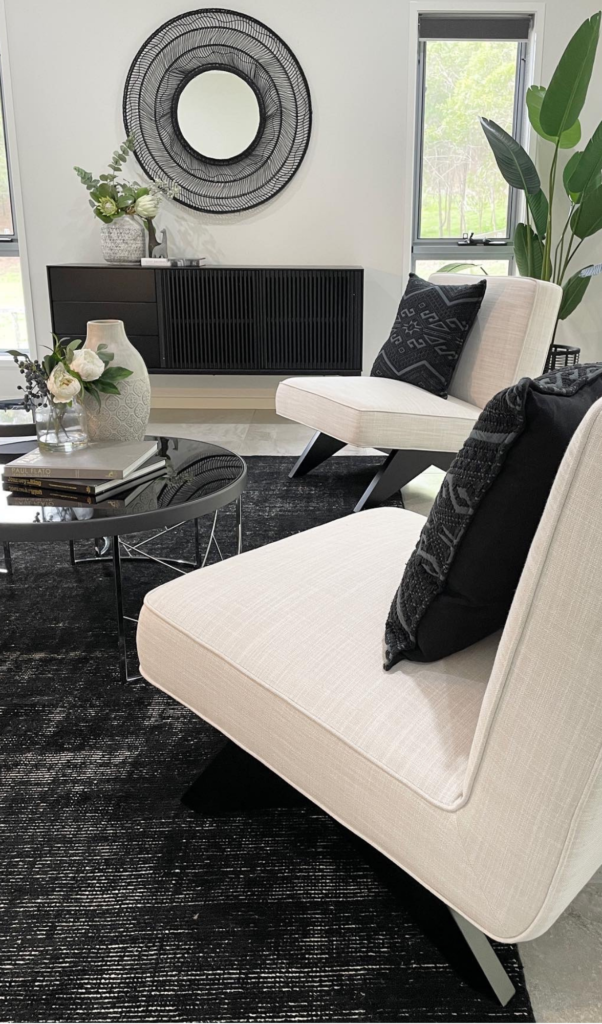 two white lounge chairs photographed in a monochromatic style with black mirror in the background, black console table, black coffee table and black rug