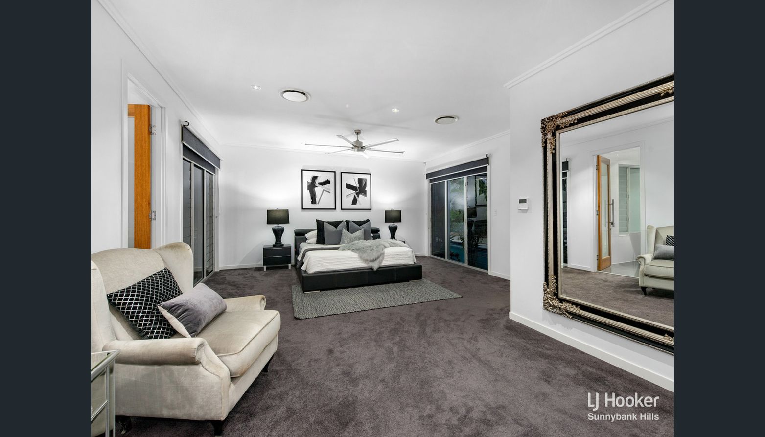 master bedroom with a black bed, grey cushions and a grey faux-fur throw, black bedside tables and lamps, two black and white artworks on the wall and a velvet cream chair at the front