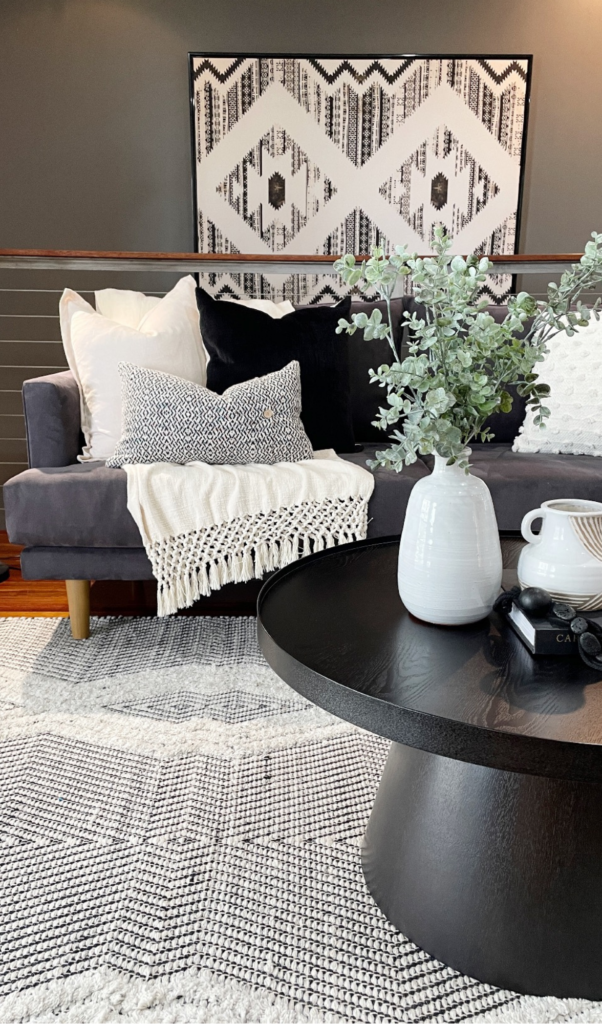 black coffee table with black and white accessories, dark grey sofa and a black and white tribal painting por