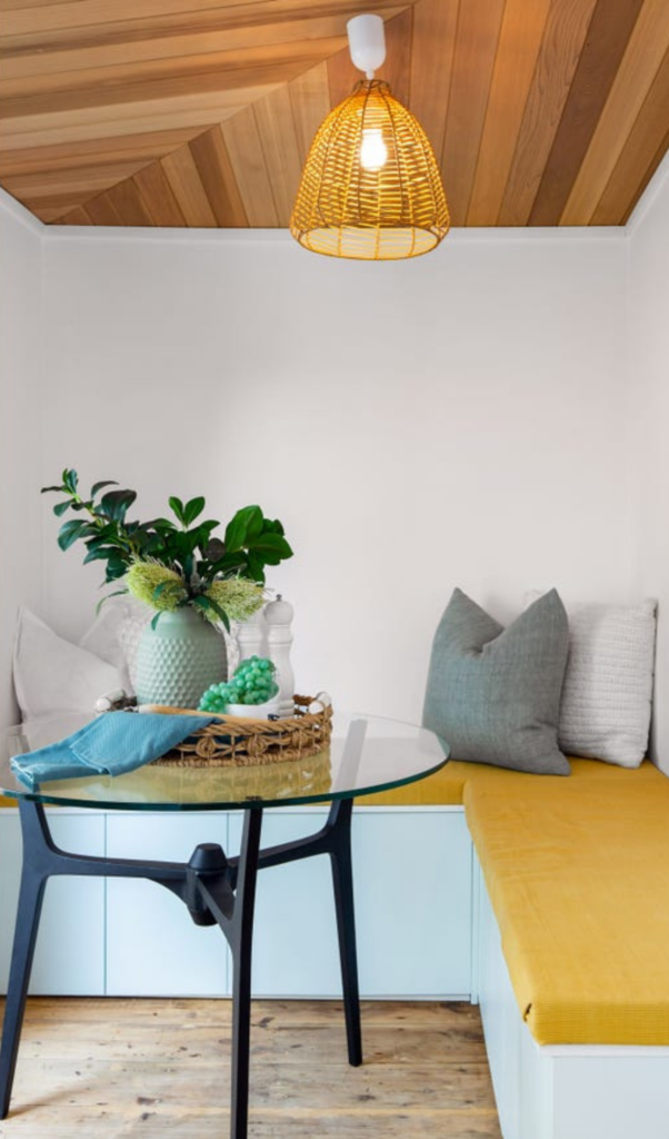 dining corner with a yellow bench seat and a glass top round dining table