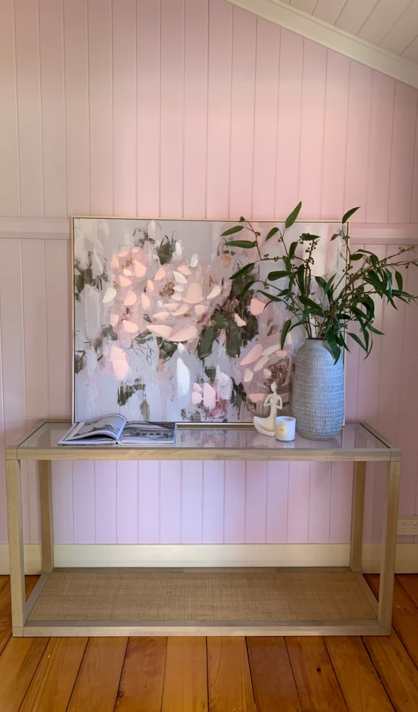 pastel pink wall with a console table styled with a floral artwork, vases and decorations